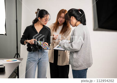 A professional Asian female photographer talking with assistants, preparing before a shooting. A professional Asian female photographer talking with assistants, preparing before a shooting. 112954202