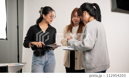 A professional Asian female photographer talking with assistants, preparing before a shooting. 112954203