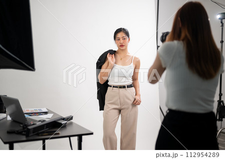 A professional photographer is taking pictures of an attractive young Asian female model in a studio A professional photographer is taking pictures of an attractive young Asian female model in a studio 112954289