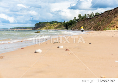 Woman alone walking along the seashore on sunny day. Big sand dunes with pine trees and cloudy sky. Woman alone walking along the seashore on sunny day. Big sand dunes with pine trees and cloudy sky. 112957197