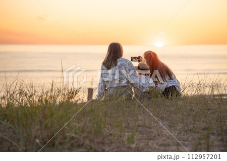 Back view of two caucasian female friends and a child making selfie at sunset on the Baltic seashore 112957201