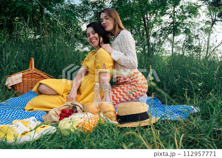 Two girls on a date sit on a blue blanket for a picnic in nature 112957771