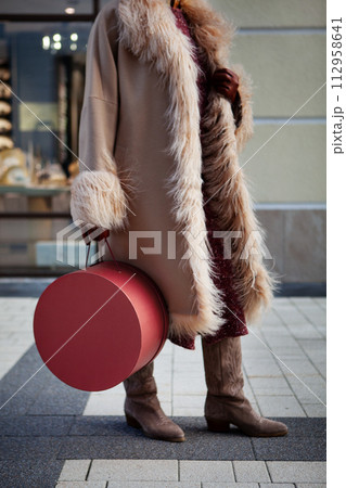Fashion woman in city, dressed in a long beige coat, Cossack boots and original mock up handbag box. Street style trend for mature women 112958641