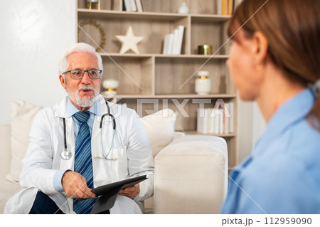 Senior man doctor examining young woman in doctor office clinic or at home. Girl patient and doctor have consultation in hospital room. Medicine healthcare medical checkup. Visit to doctor 112959090