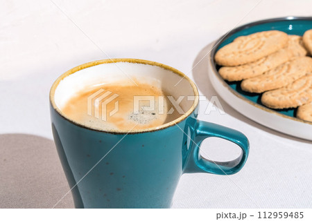 Fresh Coffee in a Blue Mug Beside Crispy Cookies on a Sunny Day 112959485