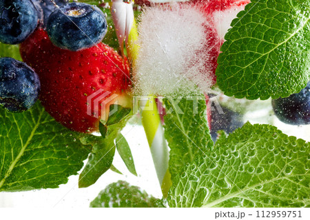 Close-up of fresh green mint leaves, strawberries and blueberries in water. Texture of cooling sweet summer's drink with macro bubbles. Lemonade. 112959751