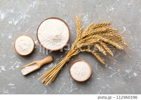 Flat lay of Wheat flour in wooden bowl with wheat spikelets on colored background. world wheat crisis 112960396