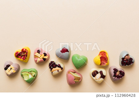 chocolate sweets in the form of a heart with fruits and nuts on a colored background. top view with space for text, holiday concept chocolate sweets in the form of a heart with fruits and nuts on a colored background. top view with space for text, holiday concept 112960428