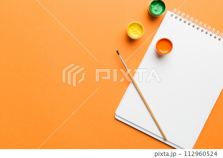 Album pages and paints, pencils, brush on a colored background. Top view with empty space. workplace for creativity. home teaching concept drawing Album pages and paints, pencils, brush on a colored background. Top view with empty space. workplace for creativity. home teaching concept drawing 112960524
