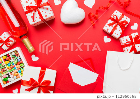 top view photo of st valentine day decor shopping, bag, wine, bottle, envelope, gift, box, candy and red heart on colored background with empty space. Frame background 112960568