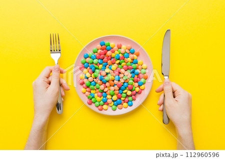the girl holds cutlery in her hands and eats sweets in a plate. Health and obesity concept, top view on colored background the girl holds cutlery in her hands and eats sweets in a plate. Health and obesity concept, top view on colored background 112960596