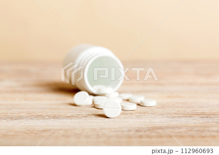 Medicine bottle and white pills spilled on a light background. Medicines and prescription pills flat lay background. White medical pills and tablets spilling out of a drug bottle Medicine bottle and white pills spilled on a light background. Medicines and prescription pills flat lay background. White medical pills and tablets spilling out of a drug bottle 112960693