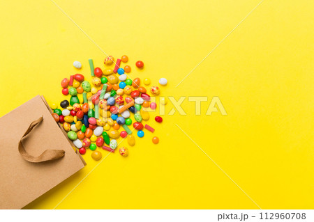 shopping paper gift bag in corner full of assorted traditional candies falling out on colored background with copy space. Happy Holidays sale concept shopping paper gift bag in corner full of assorted traditional candies falling out on colored background with copy space. Happy Holidays sale concept 112960708