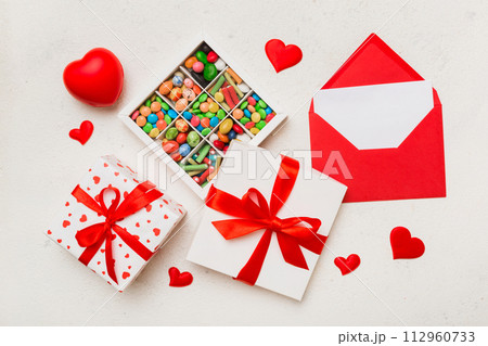 Red envelope with candy and gift box and Valentines hearts on colored background. Flat lay, top view. Romantic love letter for Holiday concept Red envelope with candy and gift box and Valentines hearts on colored background. Flat lay, top view. Romantic love letter for Holiday concept 112960733