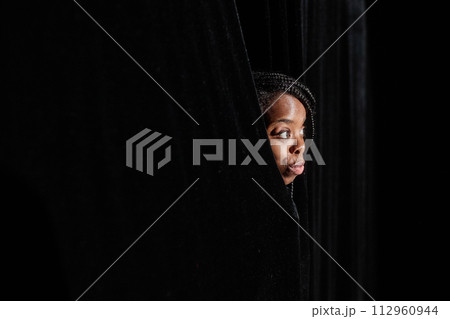 Young African American woman peeking from curtains looking at theater stage, copy space Young African American woman peeking from curtains looking at theater stage, copy space 112960944