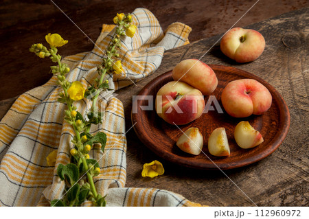 Clay plate with cut and whole saturn peaches or flat peaches on wooden background with yellow kitchen towel.. Clay plate with cut and whole saturn peaches or flat peaches on wooden background with yellow kitchen towel.. 112960972