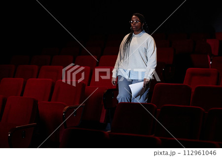 Dramatic portrait of female artist walking towards stage in empty theater audience with low light copy space 112961046