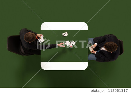 Aerial view photo of two men in smart casual attire playing game of cards sitting at common table against green background. Aerial view photo of two men in smart casual attire playing game of cards sitting at common table against green background. 112961517