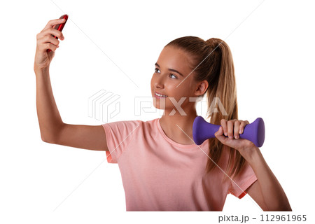 Portrait of beautiful young fit girl making selfie with smartphone and holding dumbbells isolated on white background 112961965