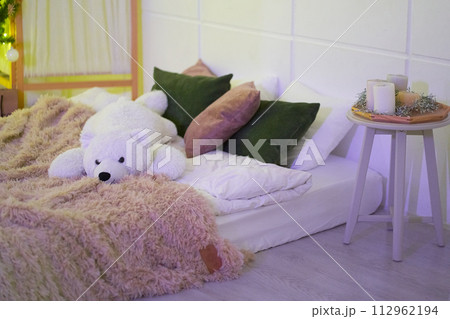 Modern interior design of bedroom with orthopedic, comfortable mattress, green, white, brown pillows, brown soft fluffy blanket, white teddy bear, white table with candles. Background with copy space. 112962194
