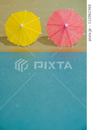 Abstract beach with glitter paper sand and water and cocktail umbrellas. Summer aesthetic mockup template background on a tropical beach holiday Abstract beach with glitter paper sand and water and cocktail umbrellas. Summer aesthetic mockup template background on a tropical beach holiday 112962368