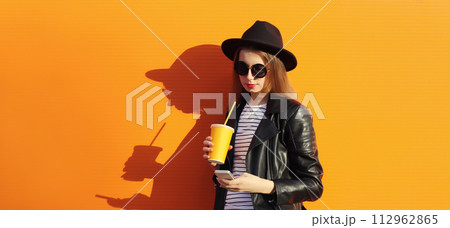 Portrait of modern stylish young woman with mobile phone drinks coffee on orange background Portrait of modern stylish young woman with mobile phone drinks coffee on orange background 112962865