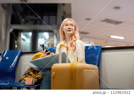 Happy young woman asian is sitting in airport near suitcase and reading map Happy young woman asian is sitting in airport near suitcase and reading map 112962922