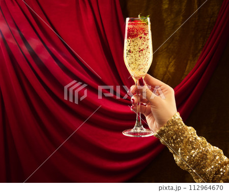 Woman's hand in festive clothes holding glass of sparkle wine decorated with strawberry. against vintage background. 112964670