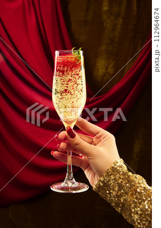 Female hand in festive clothes holding glass of sparkle wine decorated with strawberry. against vintage background. Female hand in festive clothes holding glass of sparkle wine decorated with strawberry. against vintage background. 112964674