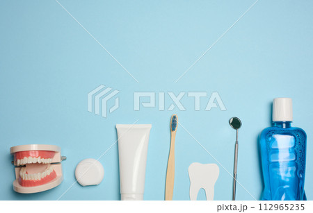 Mouthwash, toothpaste tube, dental floss and medical mirror on a blue background, oral hygiene. 112965235