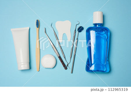 Mouthwash, toothpaste tube, dental floss and medical mirror on a blue background, oral hygiene. Mouthwash, toothpaste tube, dental floss and medical mirror on a blue background, oral hygiene. 112965319