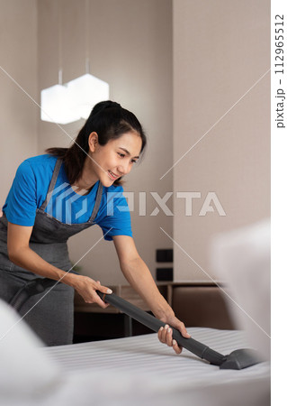 Cleaning service employee removing dirt from with professional equipment. Female housekeeper cleaning the mattress on the bed with vacuum cleaner Cleaning service employee removing dirt from with professional equipment. Female housekeeper cleaning the mattress on the bed with vacuum cleaner 112965512