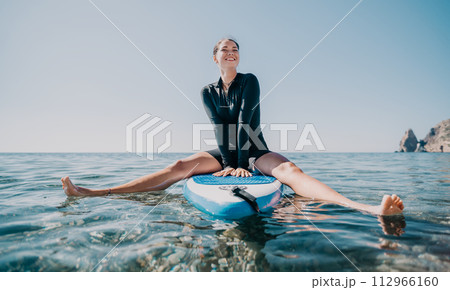 Woman sup yoga. Happy sporty woman practising yoga pilates on paddle sup surfboard. Female stretching doing workout on sea water. Modern individual female hipster outdoor summer sport activity. Woman sup yoga. Happy sporty woman practising yoga pilates on paddle sup surfboard. Female stretching doing workout on sea water. Modern individual female hipster outdoor summer sport activity. 112966160