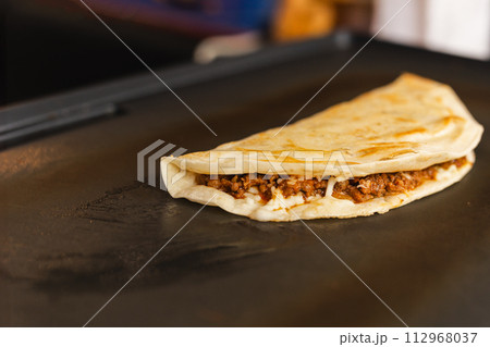 Preparing fresh quesadilla on black grill at local food market. 112968037