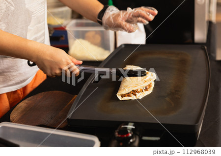 Woman preparing fresh quesadilla on black grill at local food market. 112968039