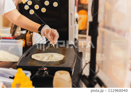 Chef sprinkles a tortilla with cheese preparing fresh quesadilla on black grill. Chef sprinkles a tortilla with cheese preparing fresh quesadilla on black grill. 112968040