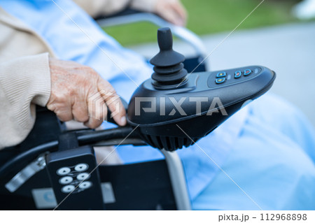 Asian senior woman patient on electric wheelchair with joystick and remote control at hospital. 112968898