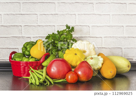 Vegetarian and healthy eating concept; heap of fresh vegetables (tomatoes, green bell peppers, green beans, zucchinis, cabage, cucumbers) on a kitchen's table 112969025