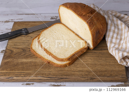Wheat (white) bread with a crispy crust on a wooden board, cut into slices. Homemade baking in rustic style. Selective focus, close-up. 112969166