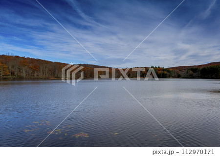 Autumn lake reflecting on a blue sky background and forest landscape 112970171