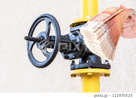 Gas valve on the pipeline of a building and ruble bills in the hand Gas valve on the pipeline of a building and ruble bills in the hand 112970525