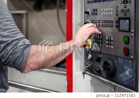 Worker pressing buttons on CNC machine control board in factory. 112971582