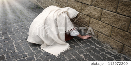 A girl in poor clothes sits on the ground 112972209