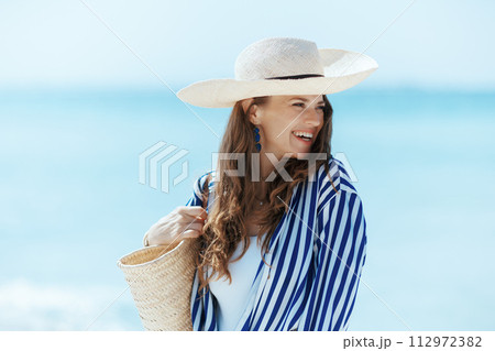 happy stylish woman on seashore with straw bag happy stylish woman on seashore with straw bag 112972382