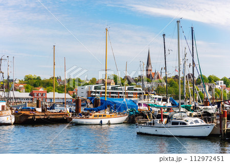 Scenic view fishing boats vessel docked Flensburg marina harbor, architectural silhouettes church cityscape background. Moored sailing vessel fjord harbour port Schleswig-Holstein Northern Germany 112972451