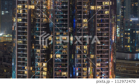 Windows of the multi-storey building of glass and steel lighting inside and moving people within timelapse 112972470