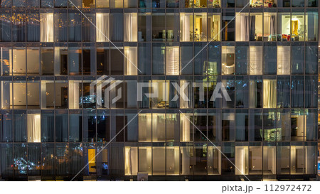 Windows of the multi-storey building of glass and steel lighting inside and moving people within timelapse 112972472