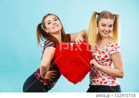 Happy two women holding heart shaped pillow Happy two women holding heart shaped pillow 112972718