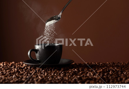 Sugar is poured into a cup of coffee. Sugar is poured into a cup of coffee. 112973744