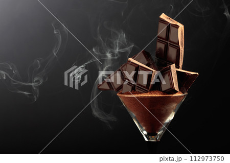 Broken black chocolate bar in glass with cocoa powder. Broken black chocolate bar in glass with cocoa powder. 112973750